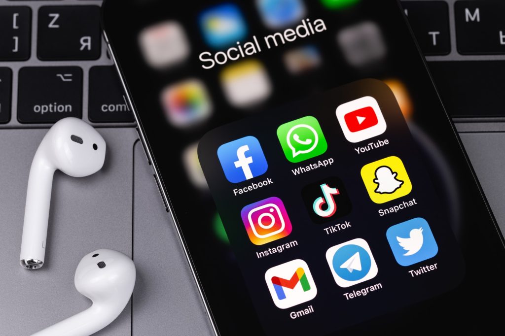 showing social media apps Facebook, WhatsApp, YouTube, Instagram, TikTok, Snapchat, Gmail, Telegram, Twitter - apps on screen smartphone iPhone with AirPods, Macbook keyboard closeup. Moscow, Russia - June 12, 2021