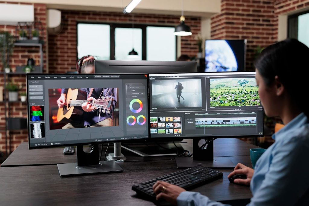 Image of a woman sitting at two computer screens, editing a video 