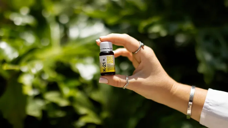 Hand holding an Immunotec bottle against green foliage