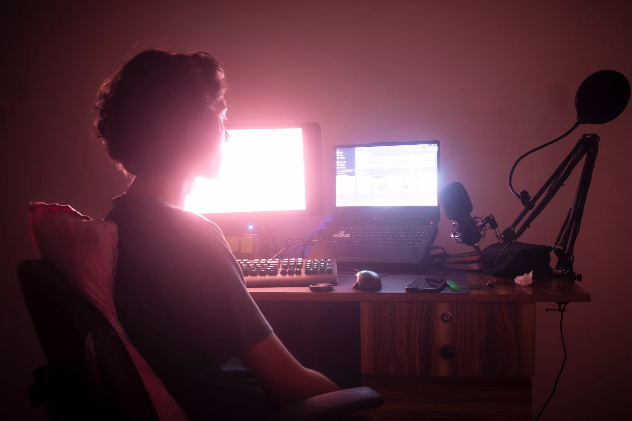 Person sitting in a darkish room with two computer screens in front of them