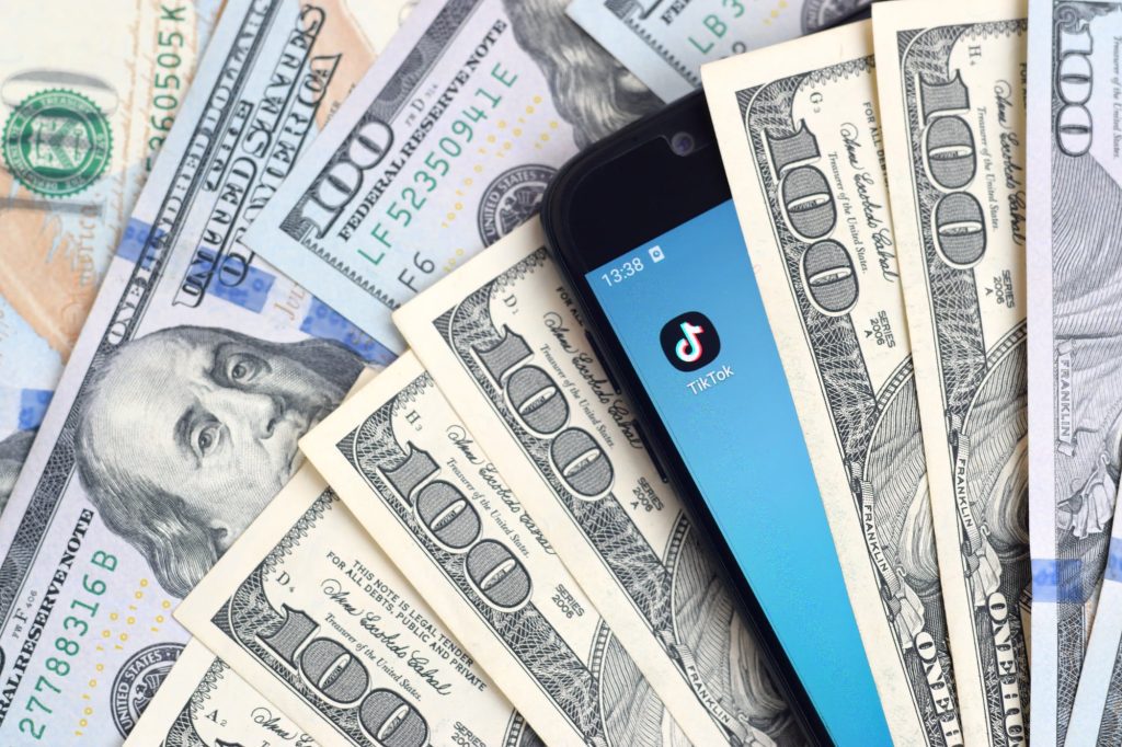 KHARKOV, UKRAINE - FEBRUARY 6, 2020: Smartphone screen with Tiktok app and lot of hundred dollar bills. Business and social networking concept