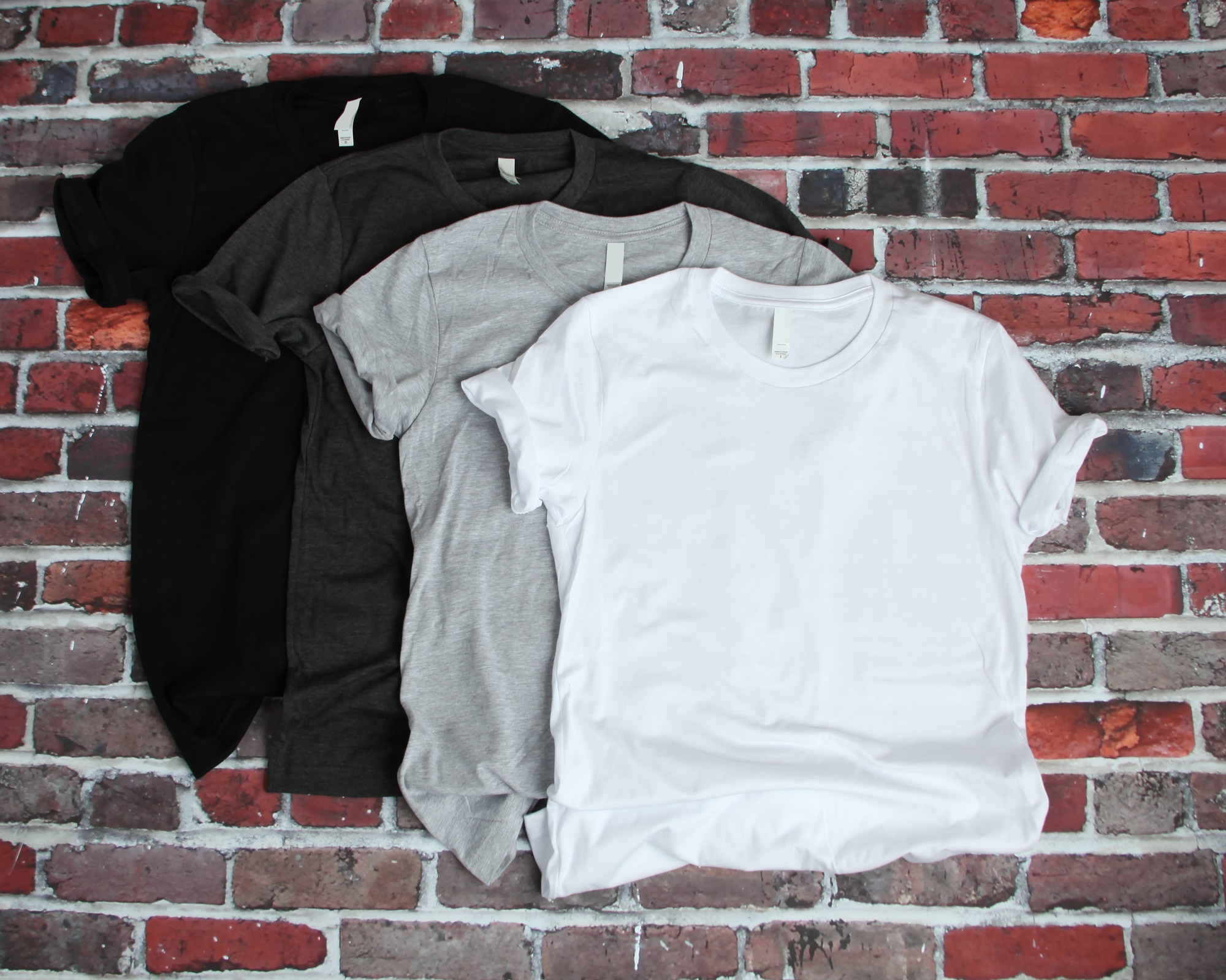 Flat lay mockup of gray, white and black tee shirts on brick background