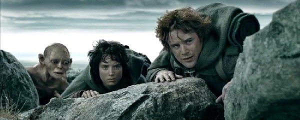 Image of 2 hobbits and a creature looking over a rock