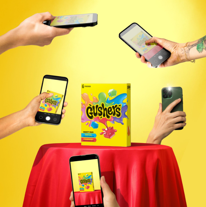 A bunch of hands holding phones taking pictures of a yellow box that says "Gushers"
